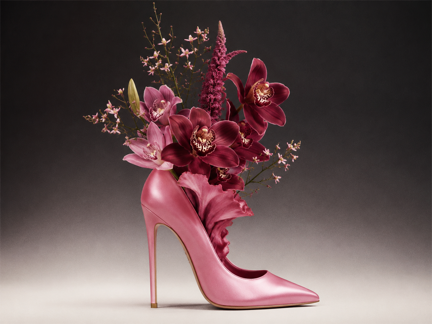 Pink stiletto boot with orchids emerging from the opening on a black-and-white gradient—surreal fashion editorial still life.
